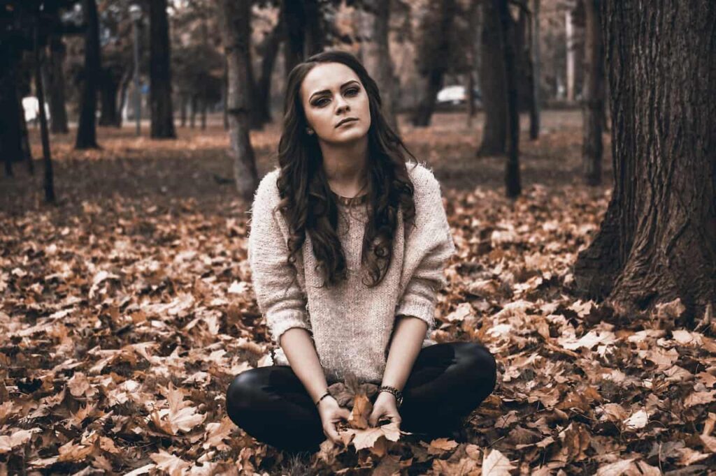 A sad girl sitting on the ground with autumn leaves