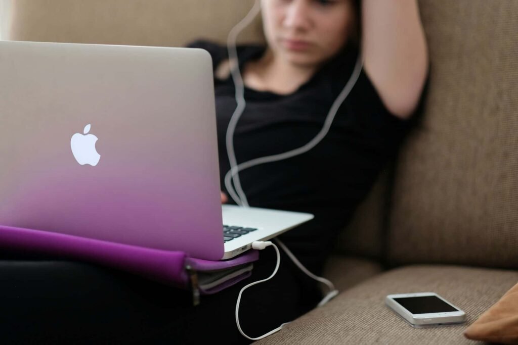A woman sitting on a couch using a laptop with earphones